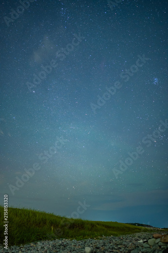 A clear star-filled night sky above a grassy coastal landscape with a rocky foreground, creating a peaceful natural nighttime scene with ample copy space.