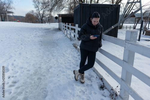 Woman holding smartphone outdoors near wooden fence in winter park