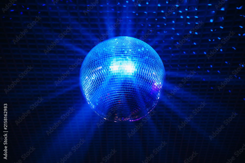 Obraz premium disco ball with mirror surface and bright rays, blue light, hanging on ceiling, night party background