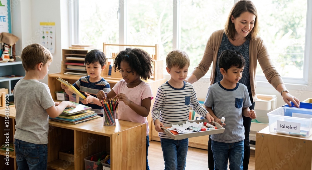 Obraz premium Group of diverse young preschool children working together with their teacher to organize books and art supplies in a bright classroom