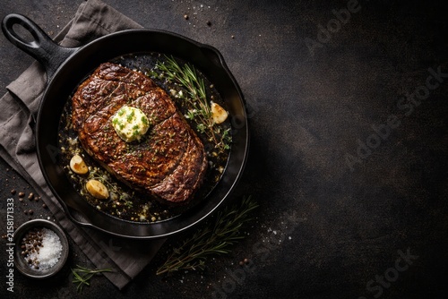 Seared ribeye steak with herb butter, garlic, and rosemary in a cast iron skillet. Rustic gourmet food composition with copy space for restaurant menu or recipe design.