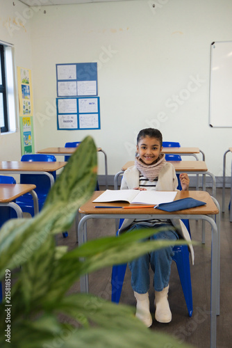 African American child student smiling at desk in class with notebook, blue folder and chunky scarf