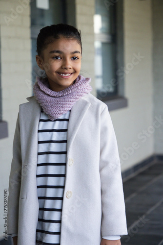 African American teenage girl standing and smiling on covered walkway wearing long coat and scarf