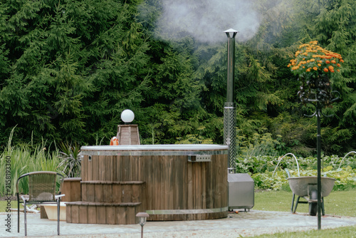 Bild auf Leinwand Empty wood-fired outdoor hot tub with smoking chimney in a landscaped garden sur