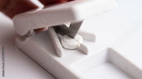 White plastic pill cutter dividing medicine tablet on a clean surface