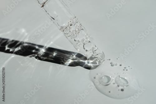Glass pipette with facial serum on a light background. Essential oil close-up in a pipette. A skin care product with hyaluronic acid in a pipette.