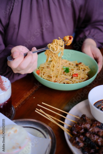 Person eating spicy noodles with a fork from a green bowl at a restaurant table
