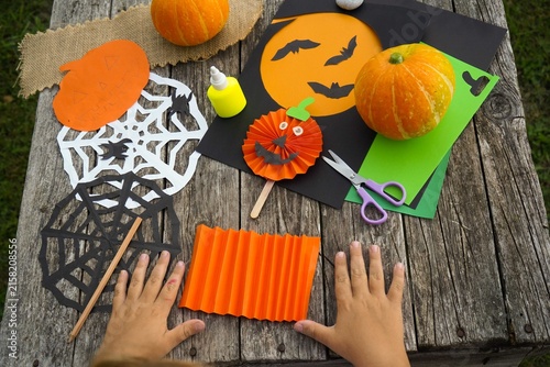 High angle view of kids hands placing on a wooden table near handmade paper pumpkin craft and Halloween decorations