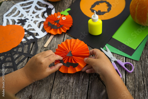 Little girl applying paper cutouts onto a wooden stick to make a creative Halloween pumpkin prop