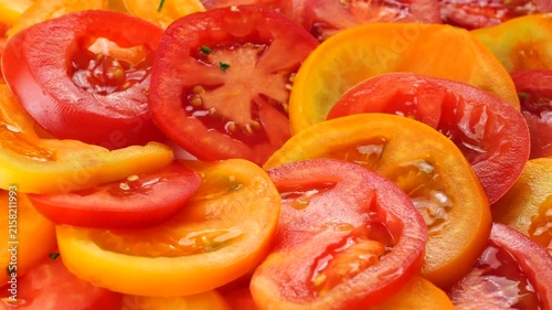 A chef sprinkles freshly chopped parsley over a vibrant salad of juicy red and yellow tomato slices arranged on a plate in a slow-motion culinary video.