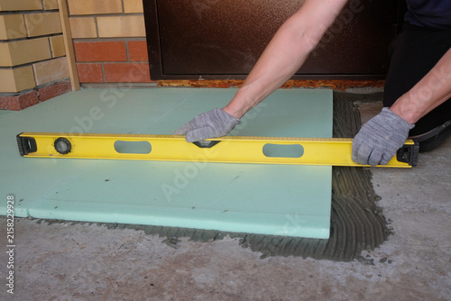 Fotografie Floor insulation: a specialist glues polystyrene foam boards to a concrete screed and checks them with a building level