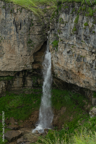 Powerful waterfall cascades down rugged cliff amid lush greenery