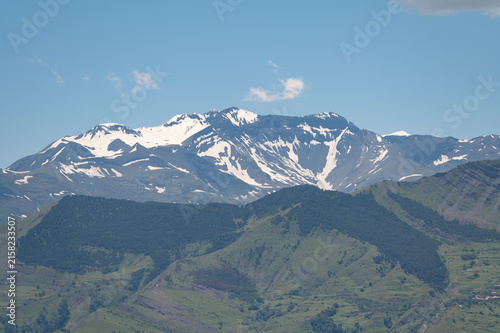 Majestic snow-capped mountains rise above rolling green hills