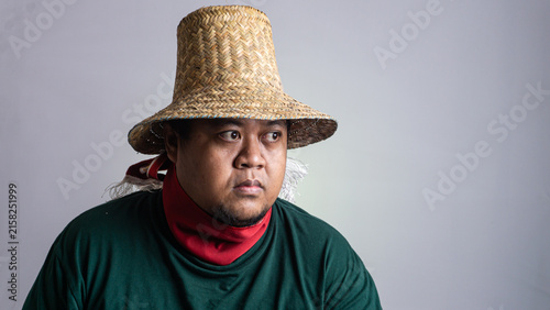 Fotografía A young Southeast Asian male gazes thoughtfully to the side wearing a traditional woven straw hat and a casual dark green long sleeved shirt