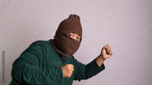 Fotografía A mysterious Southeast Asian male wears a brown full face mask while standing in a defensive boxing stance against a simple grey backdrop