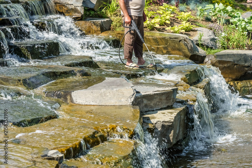 Obraz na plátne Individual standing on stone pathway near cascading water feature, using a hose