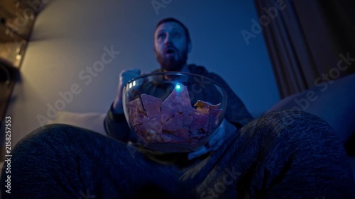 Passionate spectator reacts emotionally to a thrilling match from the sofa, cheering and shouting with snacks, capturing the excitement, suspense, tension, and unforgettable energy of live sport int.