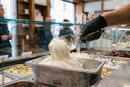 Worker hand scooping creamy white Italian gelato with metal spade in authentic gelateria