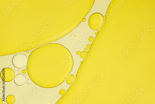 Golden cosmetic oil drops and fluid gel bubbles texture on yellow background, essence banner for skincare and beauty branding.