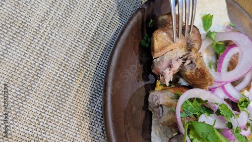 piece of juicy grilled shashlik kebab being pierced with a fork, served with sliced red onions and herbs on a plate. Delicious BBQ food concept with copy space 