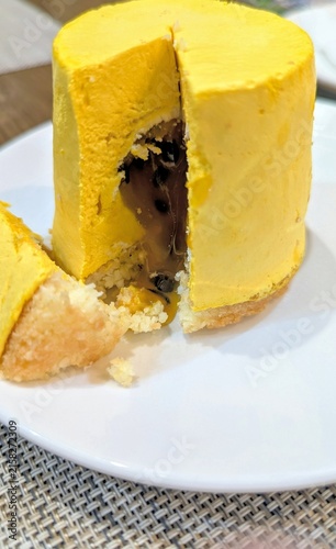 small vibrant yellow mango mousse cake with a slice cut out to reveal a dark chocolate filling on a white plate