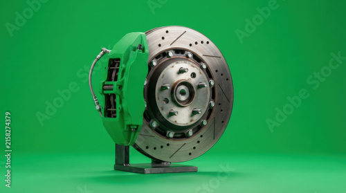 Automotive brake system with bright green caliper and perforated rotor stands on metal base against vibrant green backdrop.
