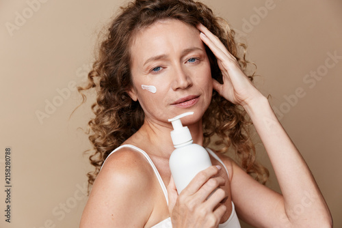 Fotografía A woman applies lotion to her face in soft studio light, showcasing skincare and moisturizer routine