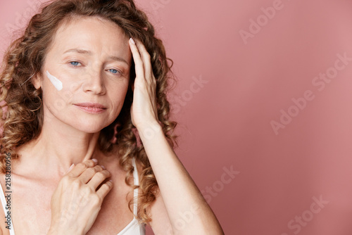 Obraz na plátně Authentic middle aged woman with natural skin without retouching applies cream on face