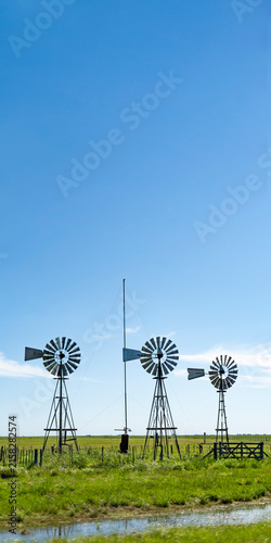 Traditional metallic windmills in rural green pasture under blue sky
