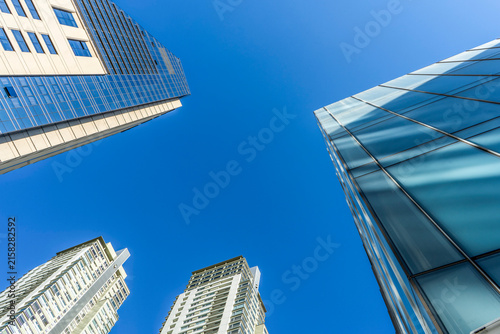 Low angle view of modern glass skyscrapers reaching towards clear blue sky