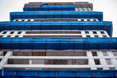 Concrete structure of urban building construction site with blue protective netting