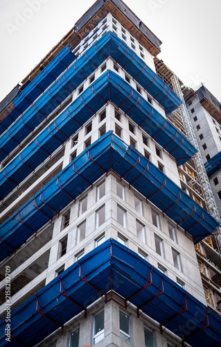 Low angle view of modern high rise building construction site with blue safety netting