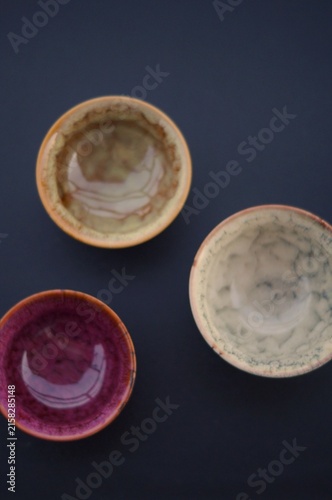 Three colorful handcrafted ceramic bowls are arranged in a top-down composition on a dark background. The image represents creative craftsmanship, visual balance, and the unique character of handmade