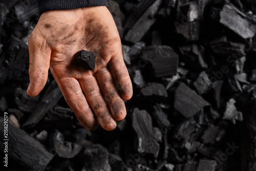 Fotografie Dirty hand holding a piece of charcoal, energy and fuel industry, environmental