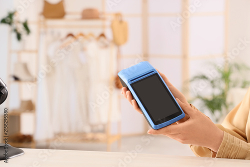 Obraz na płótnie Woman holding a blue payment terminal with a blank screen in a retail store sett