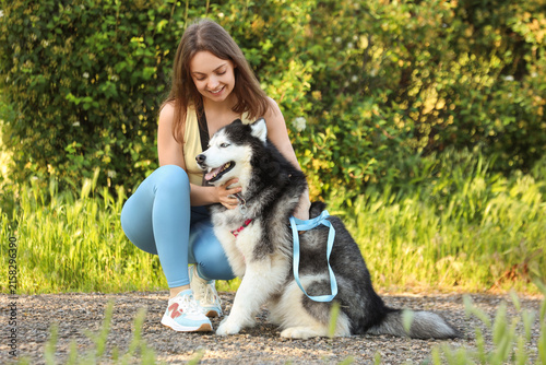 Foto Young woman crouching and petting her happy siberian husky dog outdoors in a par
