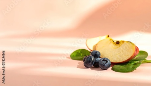 Fresh Apple Slice with Blueberries and Spinach Leaves on a Soft Pink Background.
