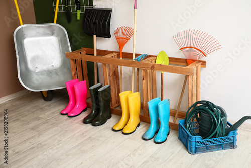 Фотография Gumboots and stand with gardening tools near colorful wall in barn