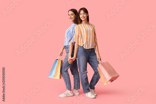 Beautiful young twin sisters with shopping bags on pink background