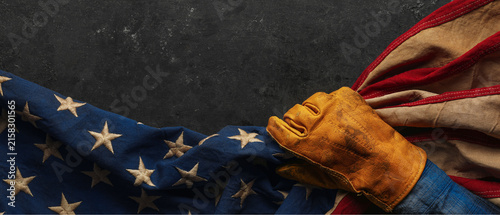 Work glove pulling the American flag with worn black background. Symbolic of hard working blue collar workers, pride in American manufacturing or products Made in USA, or to celebrate US Labor Day.