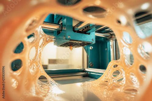 A modern three dimensional printer is actively creating a complex plastic prototype structure. Macro view focusing on the printing nozzle and extruded material. Concept for manufacturing innovation.