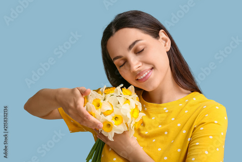 Beautiful young woman with bouquet of daffodil flowers on blue background