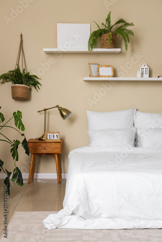 Stylish interior of bedroom with comfortable bed and lamp on bedside table ne...