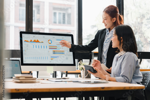 Two Asian businesswomen analyzing data and charts on a computer screen in an office