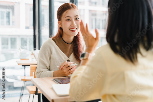 Young Asian woman smiling while talking to a female colleague in a modern cafe