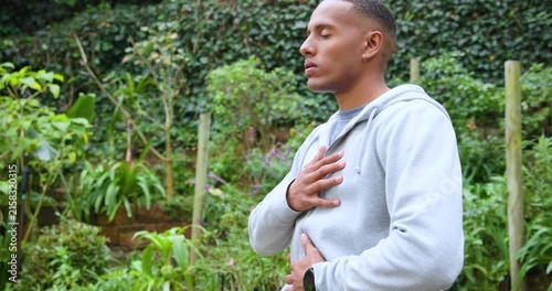 African American man placing hands on chest and belly, breathing for calm, checking watch in garden