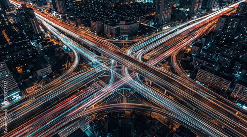 An elevated view of a complex highway interchange shows glowing light trails from moving.
