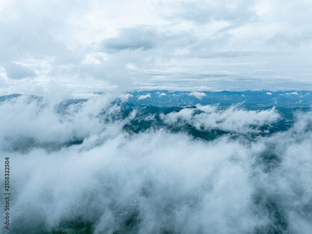 Naklejka premium A high-angle view of mountain ranges partially obscured by thick clouds and mist, showcasing a serene natural landscape.