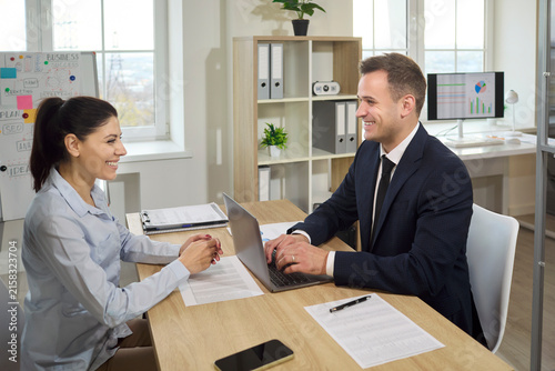Woman and man at interview meeting in office. Manager consults the candidate, using a laptop and paperwork to review experience and role fit in an office. Clear hiring and conversation concept.