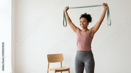 Smiling young woman exercising with a resistance band in a bright home studio.